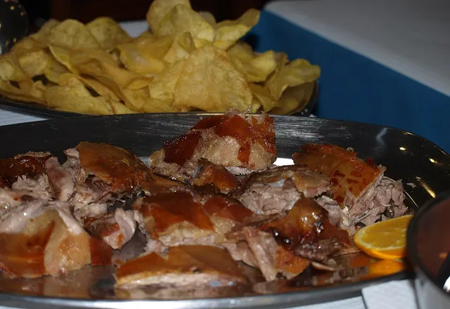 Plate of sliced roast suckling pig, with crisps and an orange slice