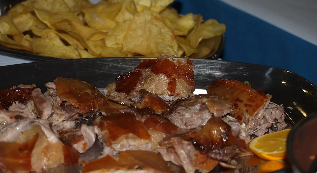 Plate of sliced roast suckling pig, with crisps and an orange slice