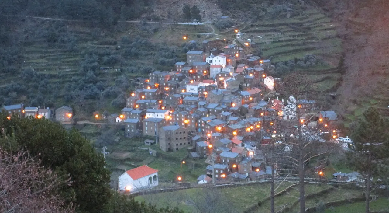 Vista aérea da aldeia de Piódão ao anoitecer, com as luzes das casas de xisto acesas