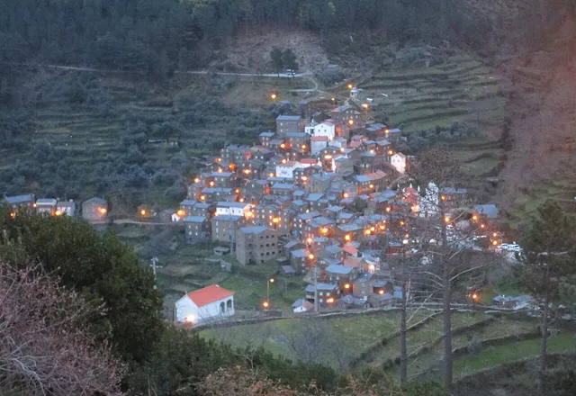 Vista aérea da aldeia de Piódão ao anoitecer, com as luzes das casas de xisto acesas